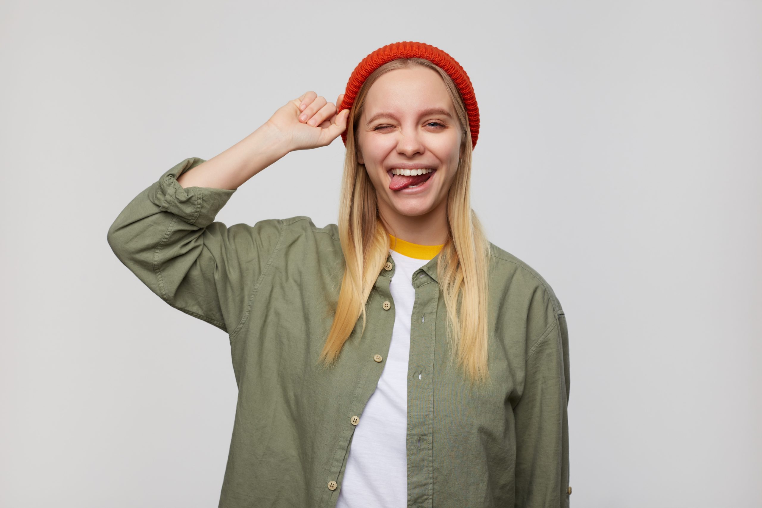 A young woman in an orange hat winks and sticks out her tongue.